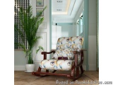 The image shows a modern living room with a wooden rocking chair in the center. The chair has a floral upholstery with a red...