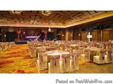 The image shows a large banquet hall with a high ceiling and a carpeted floor. The hall is set up for a formal event, with ro...