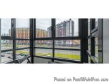 The image shows a large window with a view of a cityscape. The window is made of black metal and has multiple panes of glass,...