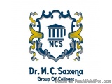 The image is a logo for the Dr. M.C. Saxena Group of Colleges. It is a shield-shaped emblem with a blue background and a whit...