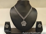The image shows a necklace and earring set displayed on a black mannequin. The necklace is made up of small silver beads and...
