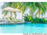 The image shows a beautiful tropical resort with a large swimming pool in the foreground. The pool is surrounded by palm tree...