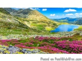 The image is a beautiful landscape of a mountain range with a lake in the foreground. The sky is blue with white clouds scatt...