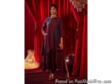 The image shows a young woman standing in front of a red curtain with a chandelier hanging above her. She is wearing a long,...