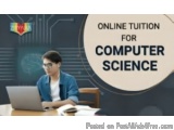 The image shows a young man sitting at a desk with a laptop in front of him. He is wearing a blue jacket and glasses and appe...