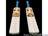 The image shows a pair of cricket bats. The bats are made of wood and have a light beige color. The handle of the bats is blu...