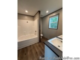This image shows a modern bathroom with a white bathtub and shower. The bathtub is on the left side of the image and has a gl...