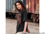 The image is a portrait of a young woman standing in front of a train. She is wearing a black t-shirt with a graphic design o...