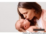 The image shows a young woman holding a newborn baby in her arms. The woman is wearing a pink cardigan and has shoulder-lengt...