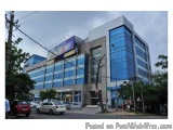 The image shows a modern building with a glass facade. The building is located on a street corner with a few cars parked on t...