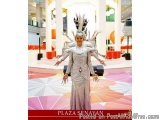 The image shows a woman standing in a shopping mall. She is wearing a long, silver dress with a high neckline and long sleeve...