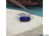 The image is a close-up of a silver ring with a large blue stone in the center. The stone appears to be a lapis lazuli, which...
