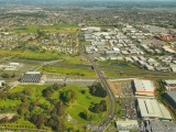 The image is an aerial view of a city with a large industrial area in the center. The city is densely populated with houses a...