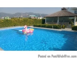 The image shows a large swimming pool with crystal clear blue water. In the center of the pool, there is a pink inflatable fl...