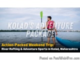 The image shows a man standing on a river raft, holding a green paddle. He is wearing a pink life jacket and shorts, and appe...