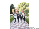 The image shows a group of five young women walking on a red and white checkered pathway in a park. They are all dressed in f...