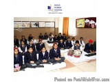 The image shows a group of school children sitting on the floor in a classroom. They are all wearing blue school uniforms and...