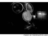 The image is a black and white photograph of a gas mask. The mask is made of metal and has two large round lenses on top. The...