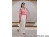 The image shows a young woman walking in a white building with a thatched roof. She is wearing a pink blouse with a floral pa...