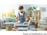 In this image, we can see a man wearing a blue apron and white gloves, working on an air conditioning unit in a living room....