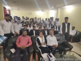 The image shows a group of people gathered in a room with a large number of people. The room appears to be a conference or me...
