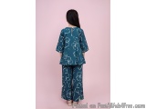 The image shows a young girl standing against a pink background. She is wearing a blue top with a white floral print on it. T...