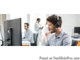 The image shows a man wearing a headset in a call center. He is sitting in front of a computer monitor and appears to be enga...