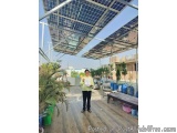 The image shows a man standing on a wooden deck with a large solar panel installation on the roof. The man is holding a certi...