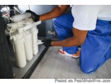 In this image, we can see a plumber working on a water filter system. The plumber is wearing a white t-shirt, blue pants, and...