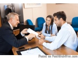 The image shows three people sitting around a wooden table in a meeting room. On the left side of the image, there is a man i...