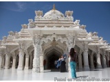 The image shows a large white temple with intricate carvings and sculptures on its façade. The temple has a dome-shaped struc...