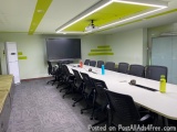 The image shows a modern conference room with a long white table in the center. The table is surrounded by black office chair...