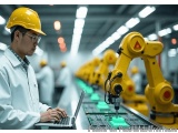 The image shows a man wearing a yellow hard hat and a white lab coat, working on a laptop in a factory. He is standing in fro...