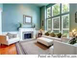 The image shows a living room with a large window on the right side. The walls are painted in a light blue color and the floo...