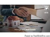 The image shows two people shaking hands over a desk with a small model of a house and a laptop in the background. The desk a...