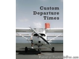 The image shows a small white airplane parked on an airport tarmac. The airplane has a red emergency light on the nose and a...