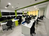 The image shows an office space with multiple computer desks and chairs arranged in rows. The desks are white and have multip...