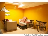The image shows a modern living room with bright orange walls and a white sofa. The sofa has a colorful throw pillow on it an...