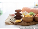 The image shows a spa-like setting with a wooden tray on a white table. On the tray, there are three small wooden bowls fille...