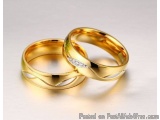 The image shows two gold wedding rings lying on a white surface. The rings are intertwined, with one ring on top and the othe...