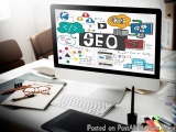 The image shows a desktop computer monitor with the word "SEO" written on the screen in bold letters. The monitor is placed o...