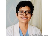 The image is a portrait of a young woman with short black hair and glasses. She is smiling and looking directly at the camera...
