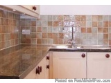 The image shows a kitchen countertop with a sink and a backsplash made of small square tiles in different shades of brown and...