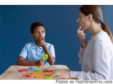 The image shows a young boy and a young woman sitting at a table with colorful plastic letters scattered across the table. Th...