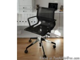 The image shows a black office chair in an office setting. The chair has a high backrest and armrests, and a swivel base with...