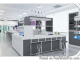 The image shows a modern laboratory setup with a large white countertop and gray cabinets. On the countertop, there are sever...
