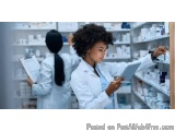 The image shows two young women in a pharmacy. They are both wearing white lab coats and are standing in front of shelves fil...