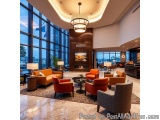 The image shows the lobby of a modern hotel. The lobby has a high ceiling with a large chandelier hanging from it. The floor...