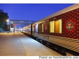 The image shows a train station at night. The train is a passenger train with a red and gold color scheme. It is parked on th...