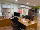 The image shows an office space with a large wooden desk in the center. The desk is surrounded by four black office chairs. O...